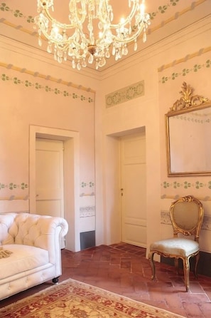 A room with a white sofa, a gold chair, a chandelier, and a patterned rug. - Residenza d'Epoca - B&B Santa Caterina (Pisa)