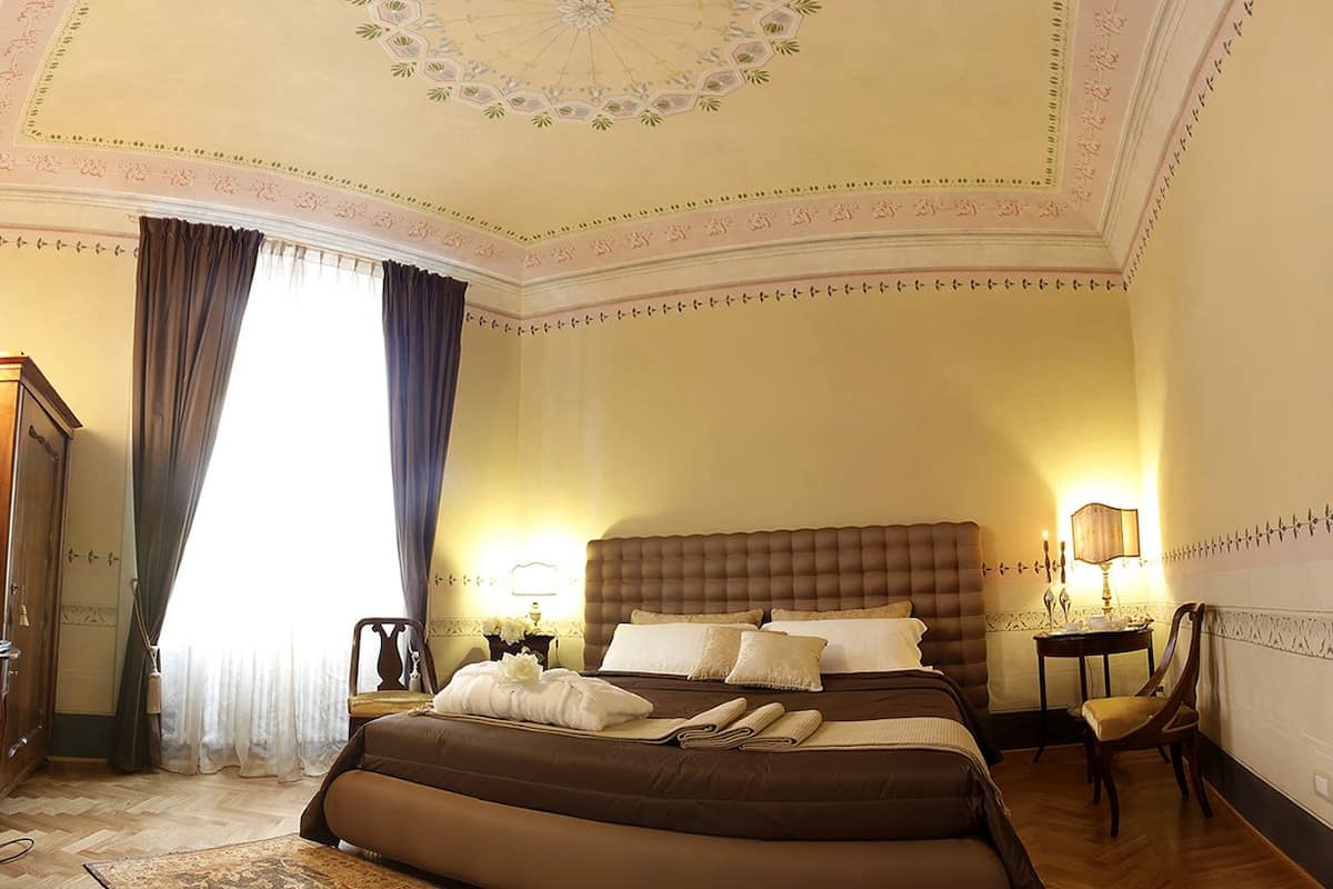A hotel room with a large bed, two bedside tables, a chair, and a wardrobe.