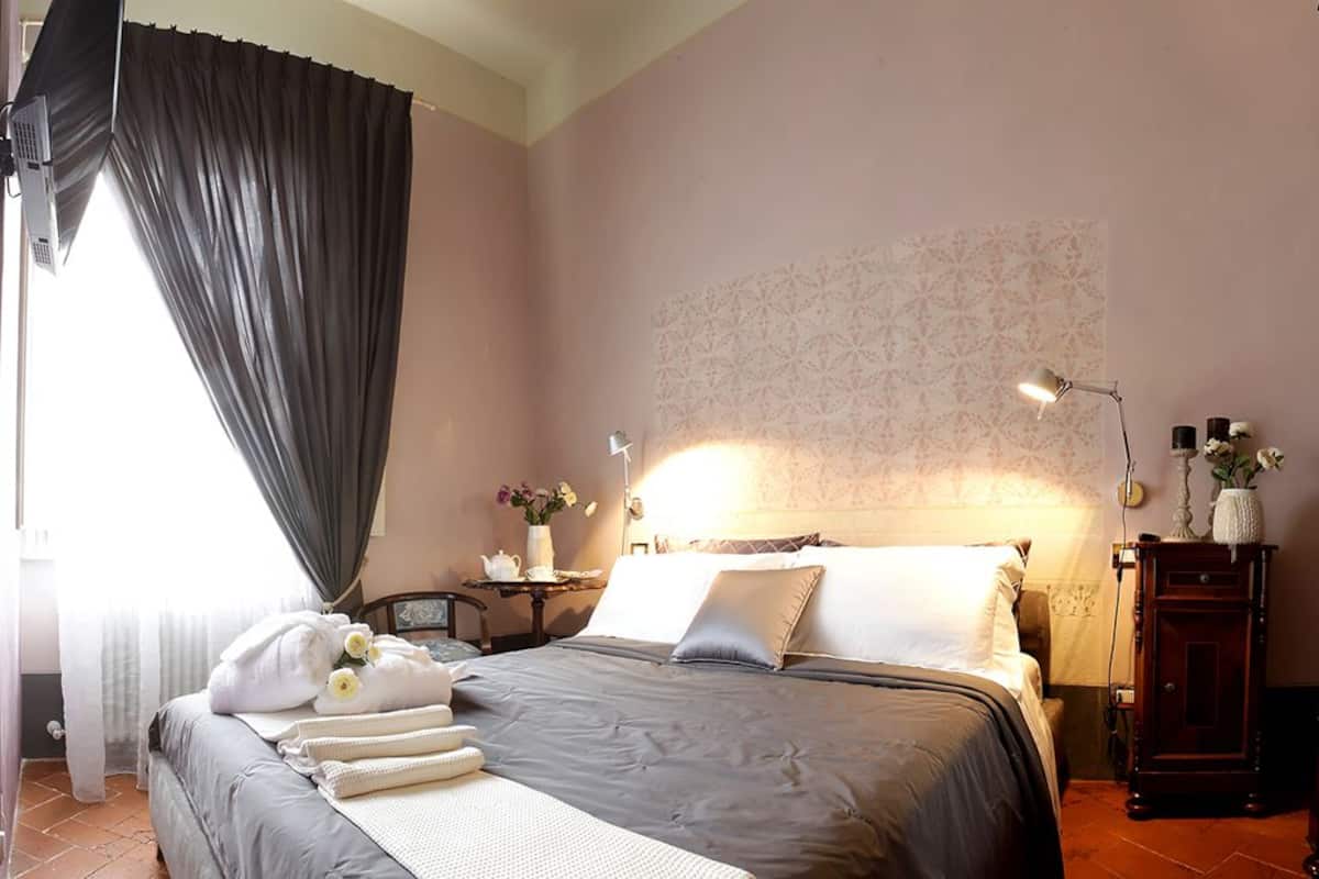 A neatly made bed with pillows and a blanket, a bedside table with a lamp, a dresser, and a mirror.
