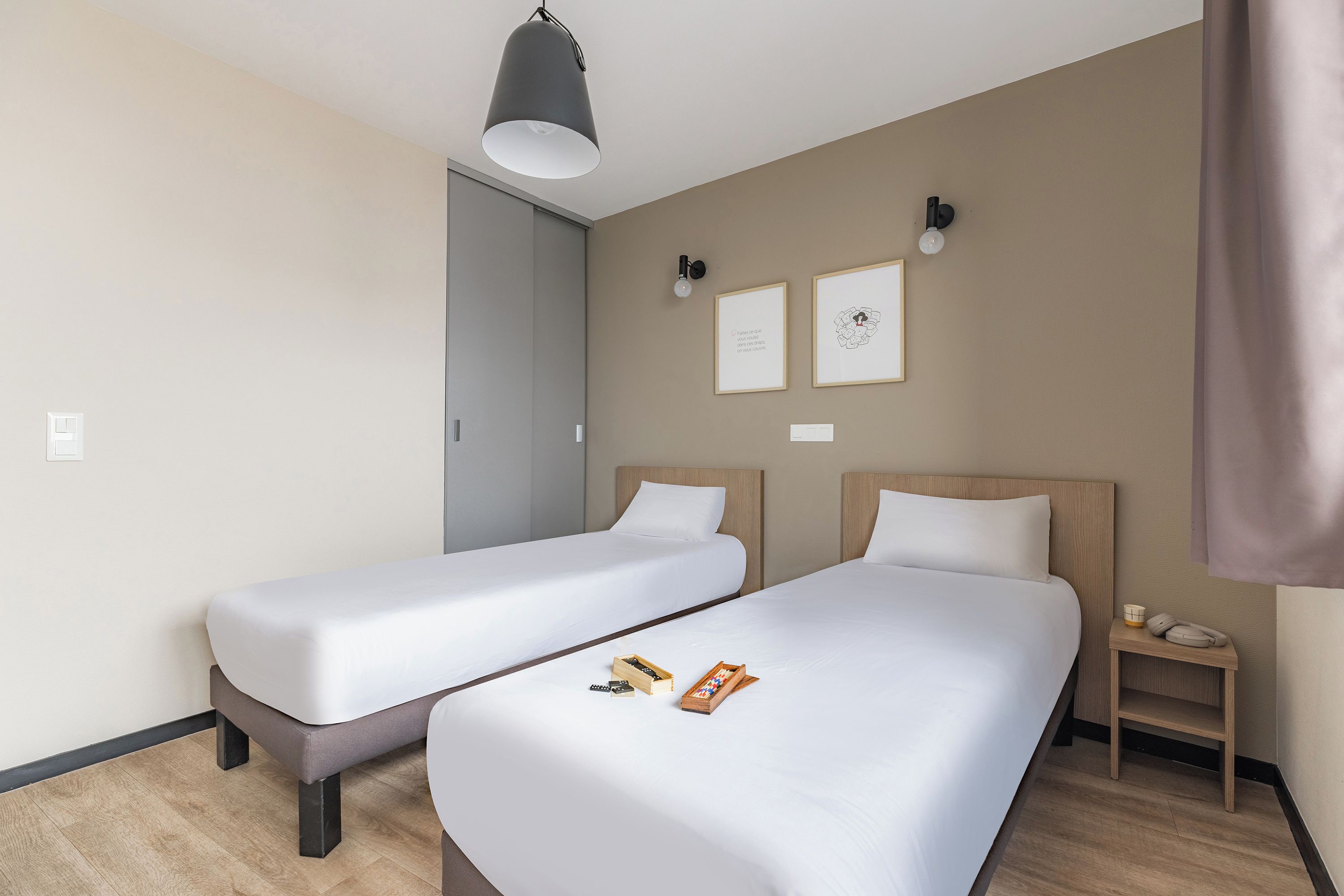 A hotel room with two single beds, a desk with a phone, and a wall-mounted light fixture.