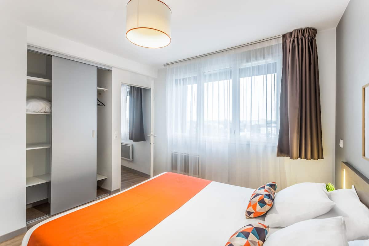 Une chambre d’hôtel avec un lit, une armoire et une fenêtre avec des rideaux.