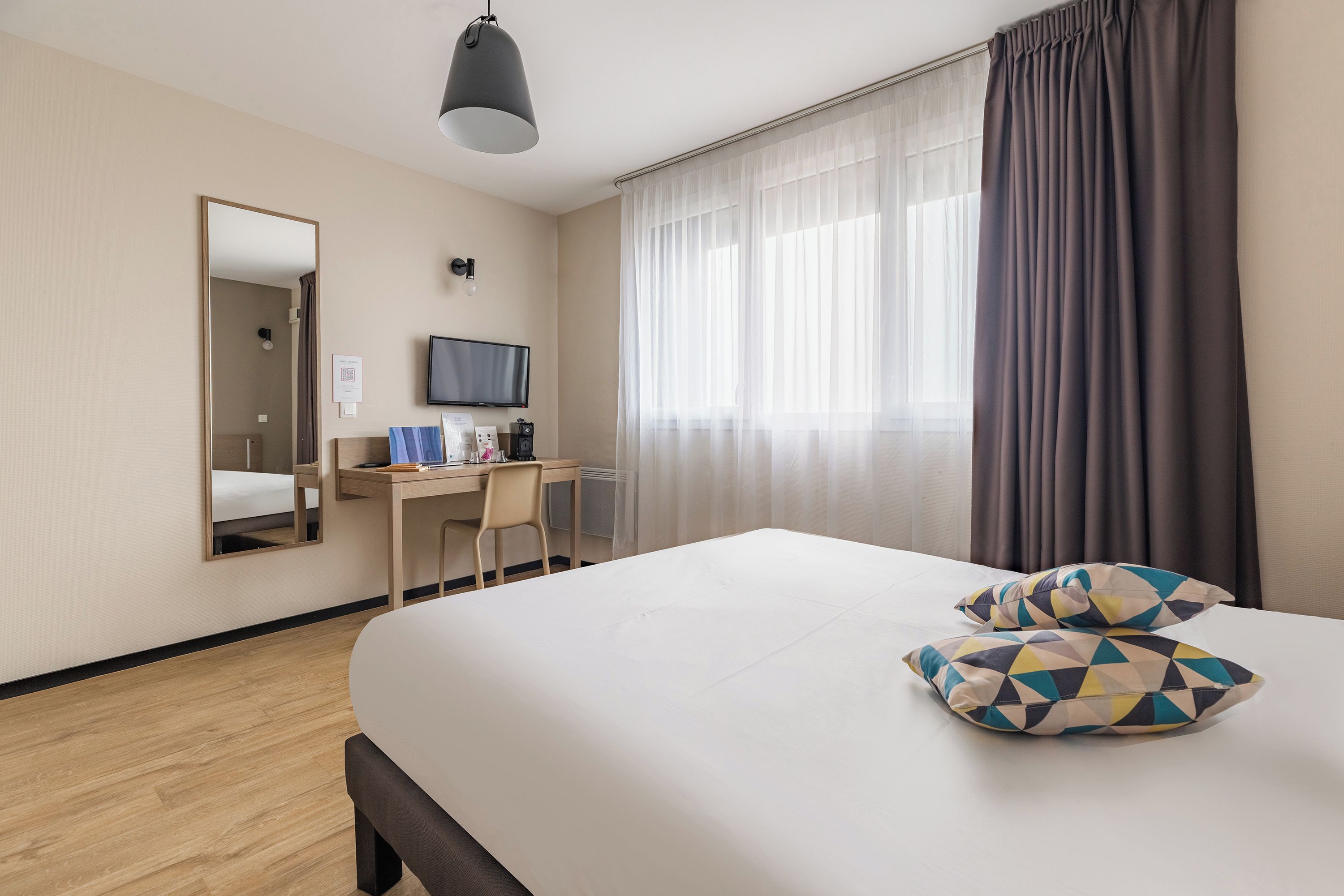 A hotel room with a bed, a desk, a chair, a television, and a window with curtains.