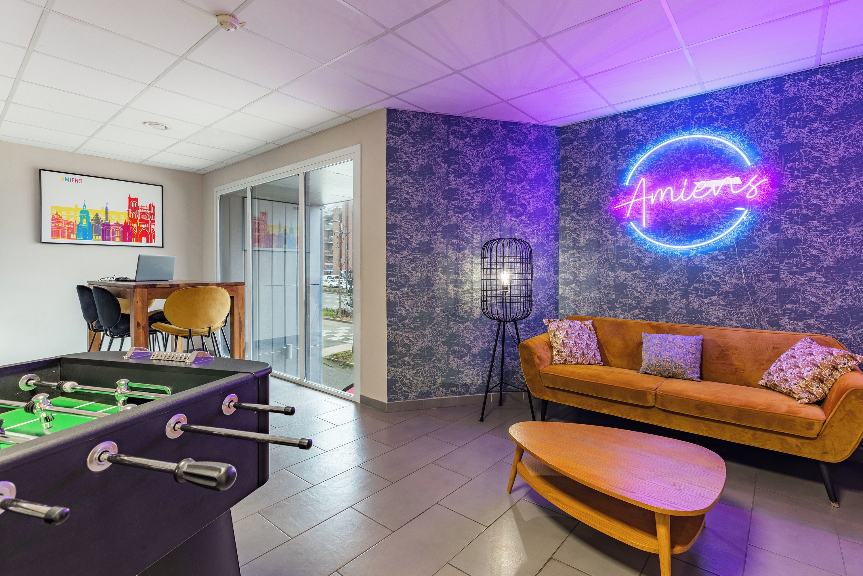 Een moderne lounge met een tafelvoetbalspel, een bank en een neonbord.