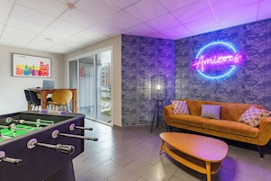 Un espacio lounge moderno con mesa de fútbol, sofá y letrero de neón.