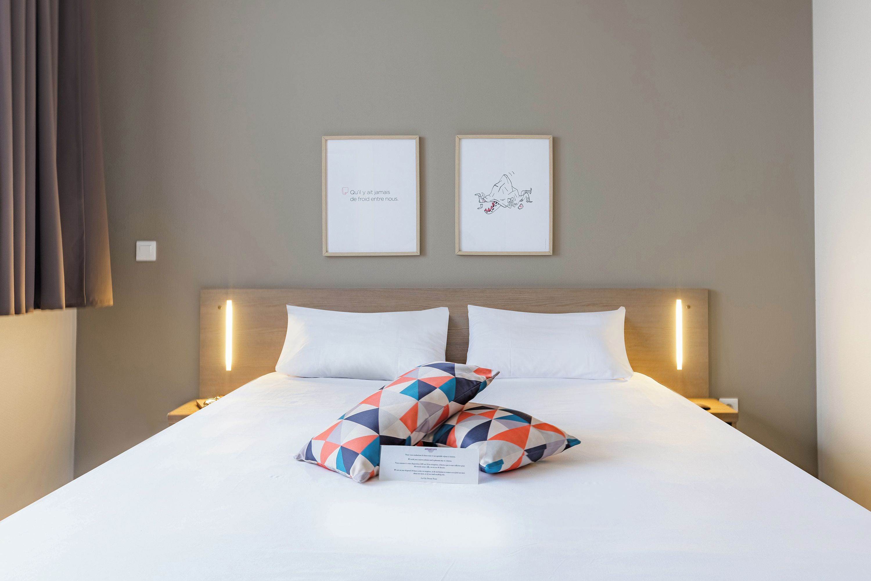 Habitación de hotel con una cama, dos mesitas de noche, un cabecero y dos cuadros enmarcados en la pared.