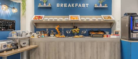 A breakfast area with a sign reading 'BREAKFAST,' a variety of fruits, and a coffee machine.
