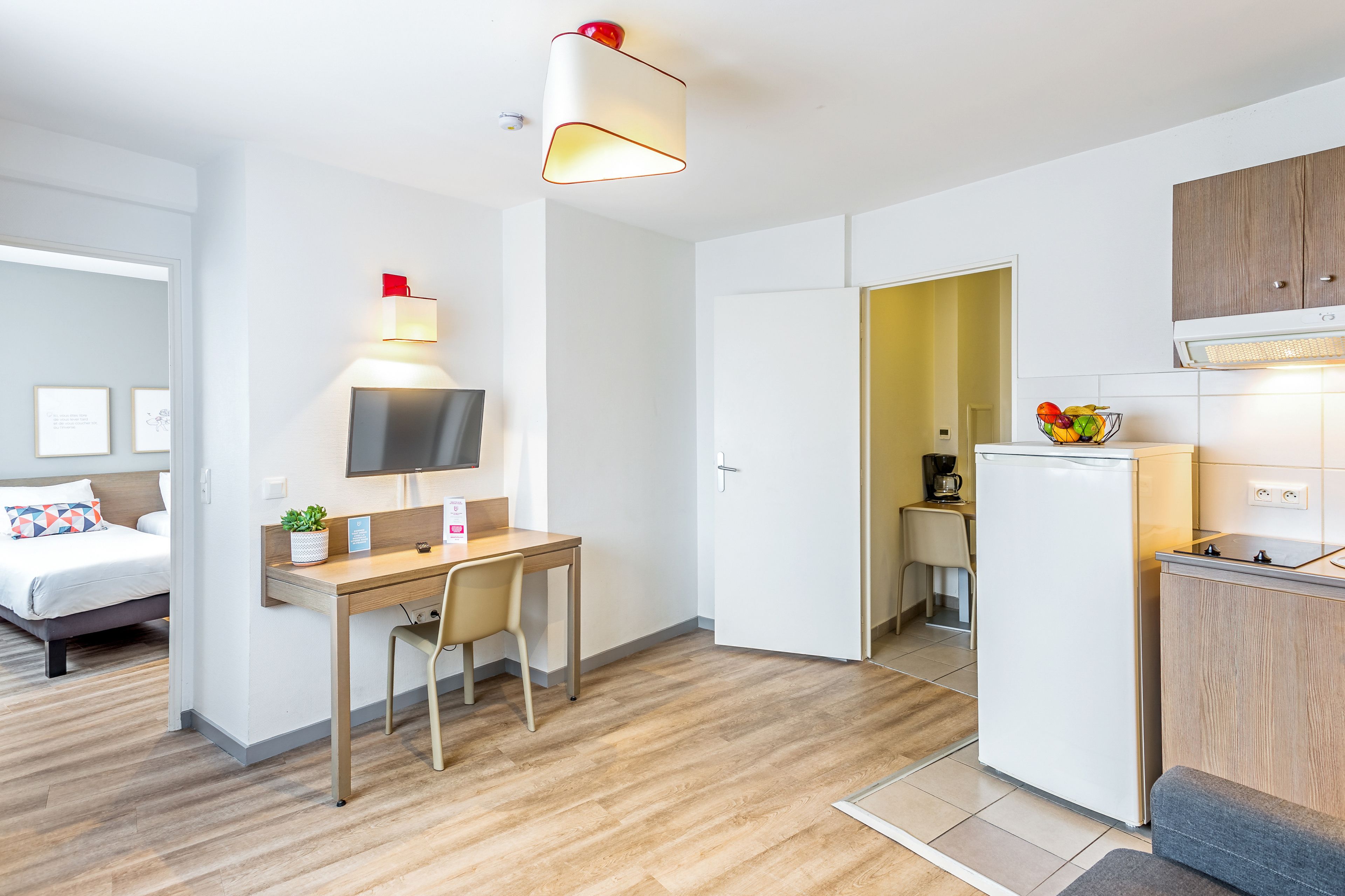 Ein modernes Hotelzimmer mit Schreibtisch aus Holz, Flachbildfernseher, Bett und Küchenzeile.