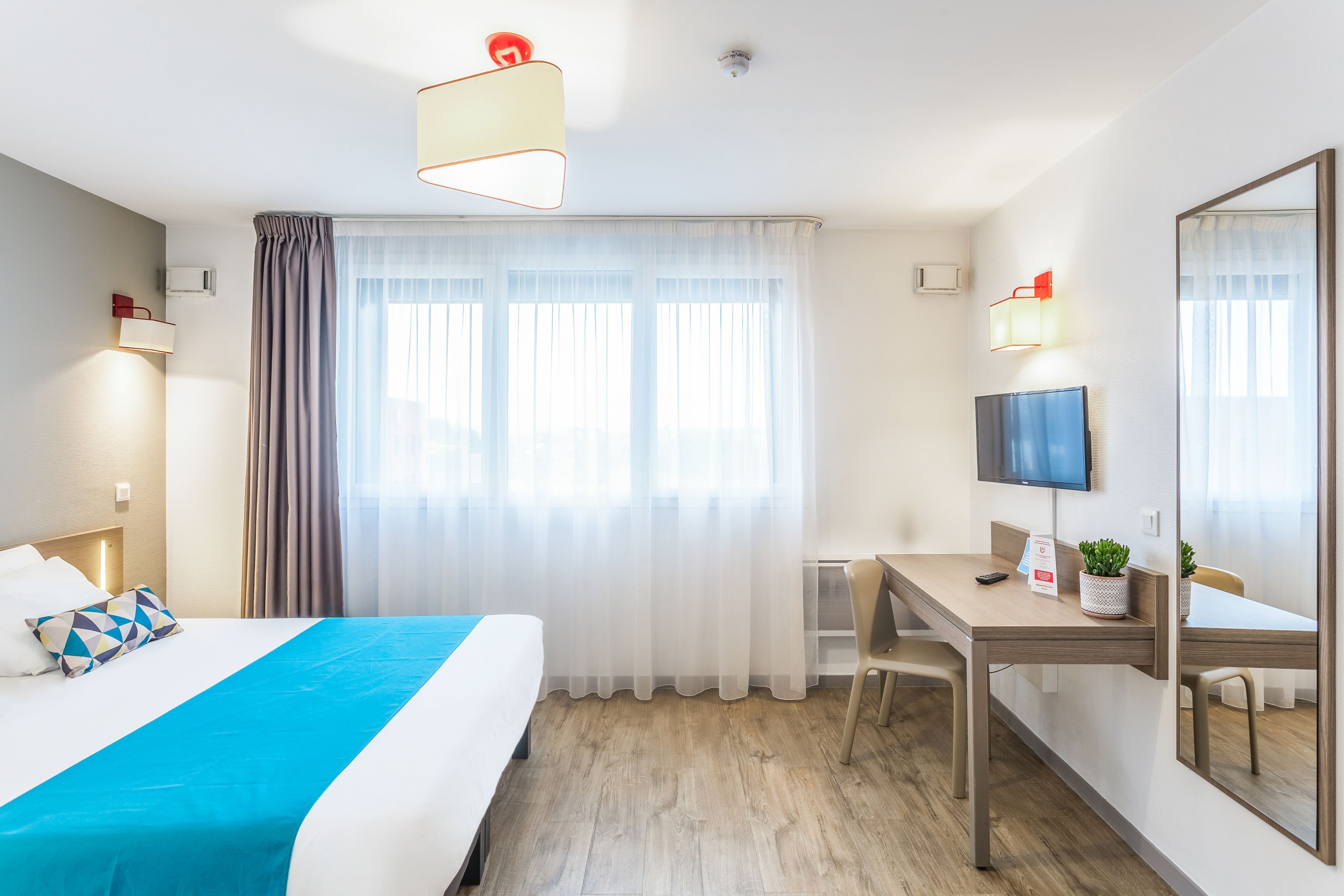 Ein Hotelzimmer mit Bett, Schreibtisch, Stuhl, Fernseher und einem großen Spiegel.