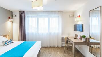 Ein Hotelzimmer mit Bett, Schreibtisch, Stuhl, Fernseher und einem großen Spiegel.