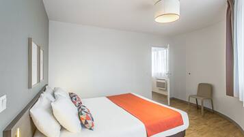 A modern hotel room with a large bed, a bedside table, a chair, and a window with curtains.