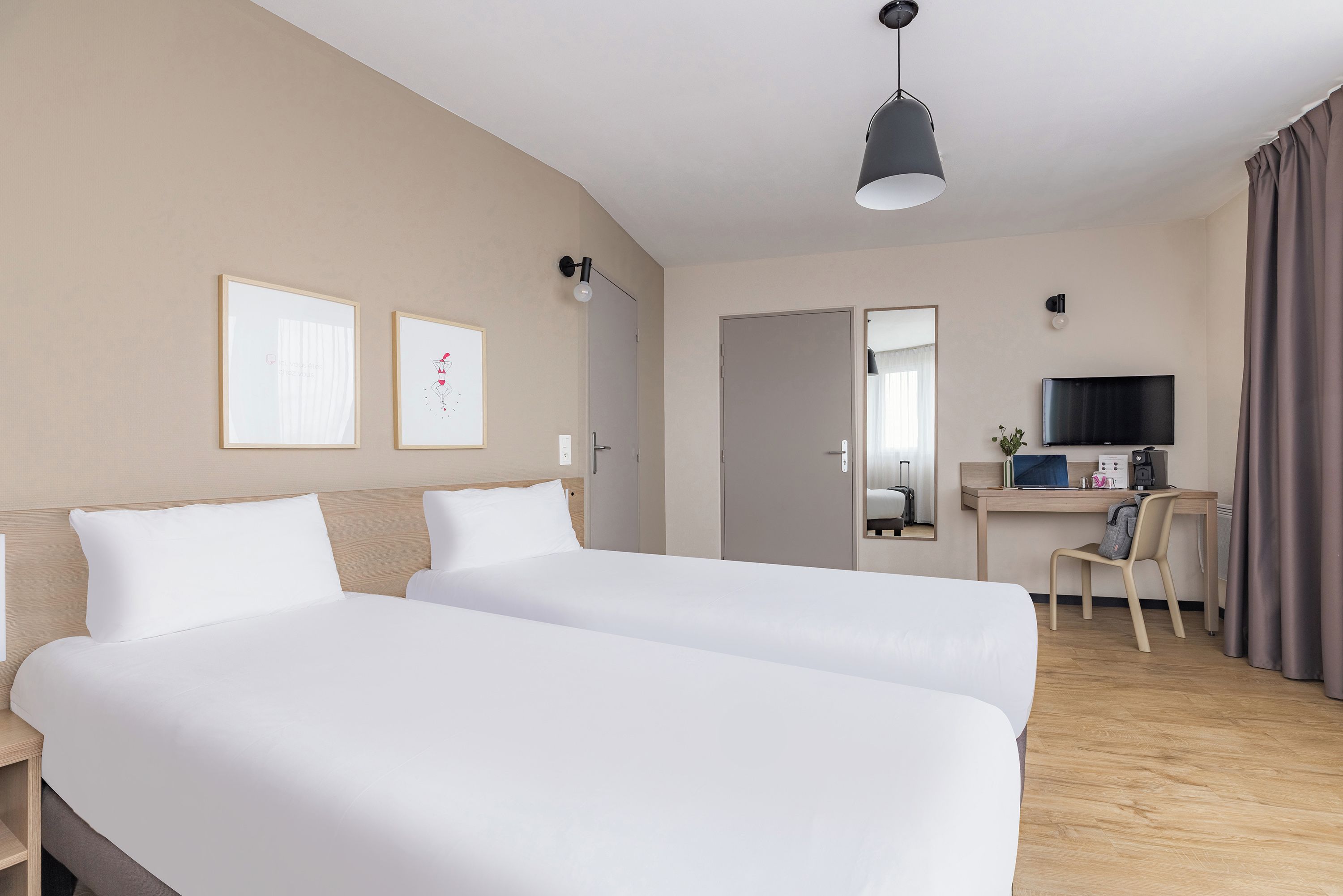 A hotel room with two beds, a desk with a computer, a TV, and a mirror.
