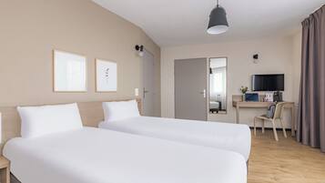 A hotel room with two beds, a desk with a computer, a TV, and a mirror.