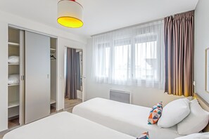 Une chambre d’hôtel avec deux lits, une armoire, un radiateur et une fenêtre avec des rideaux.