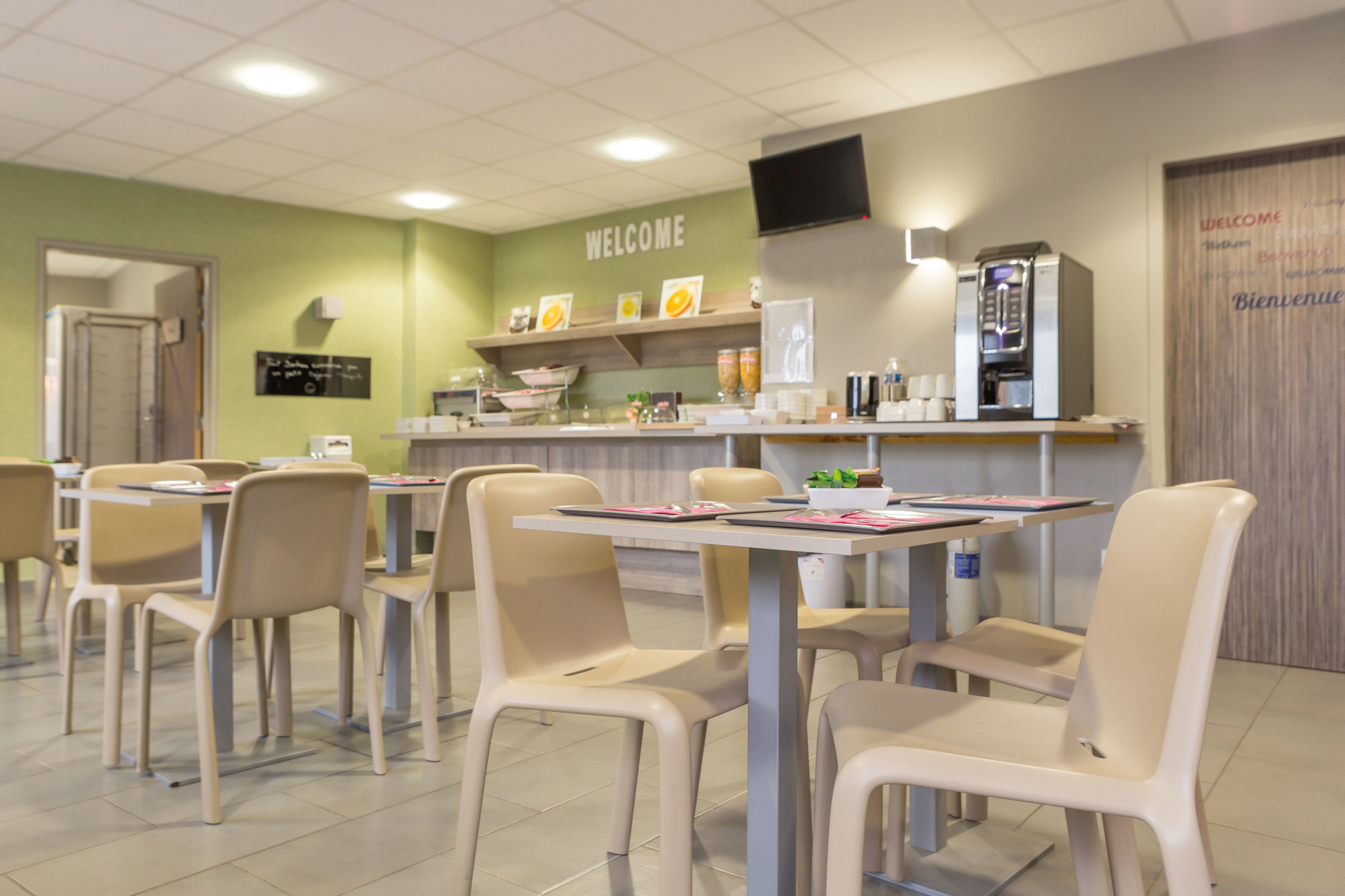 A cafeteria with tables and chairs, a coffee machine, and a welcome sign.