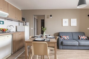 A modern kitchen with a dining area and a grey sofa.