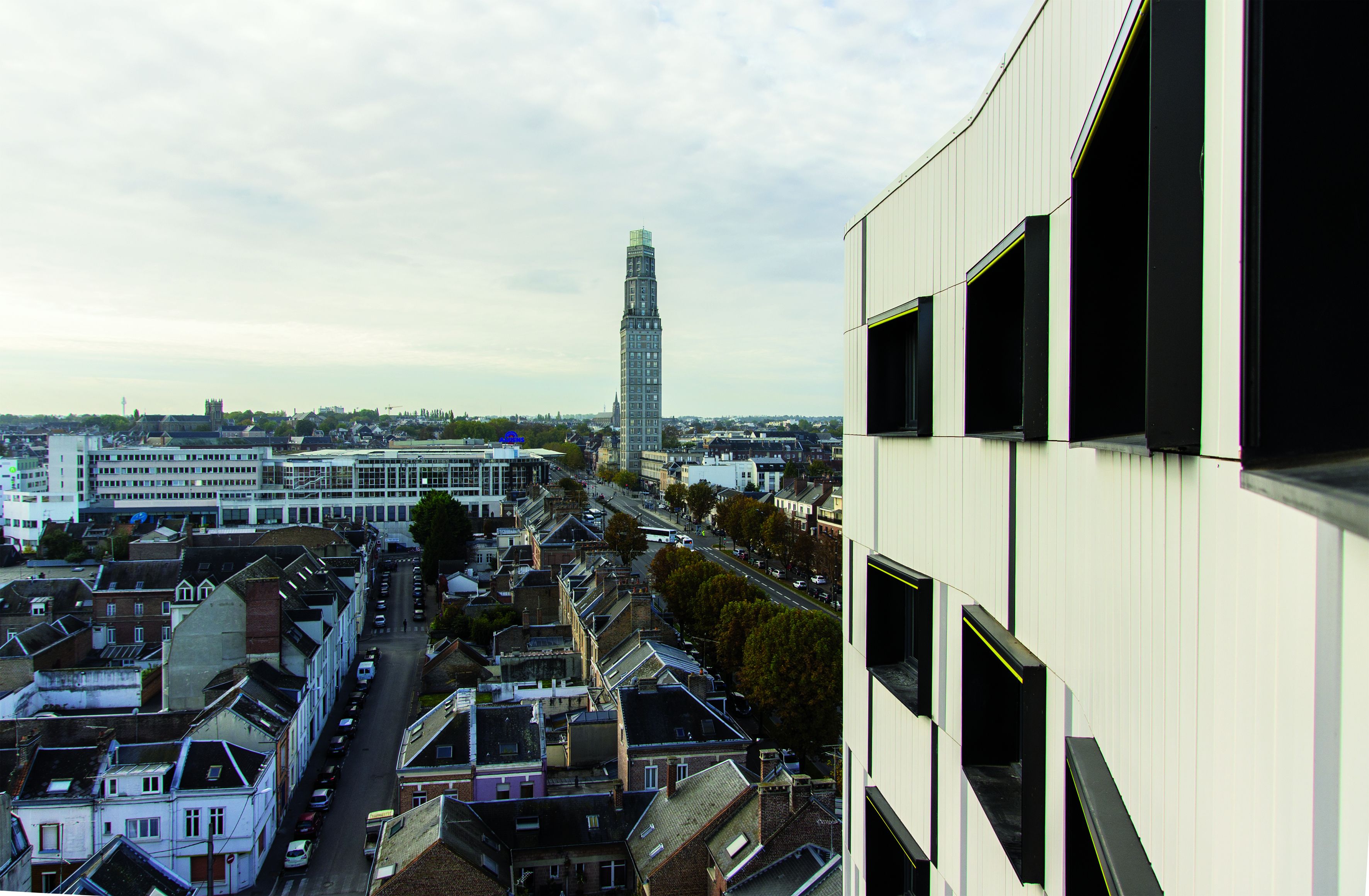 A high-rise building with a modern design, overlooking a cityscape with residential buildings and a prominent tower in the distance.