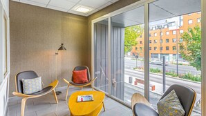 Een moderne kamer met een groot raam, twee fauteuils met kussens, een klein tafeltje met een tijdschrift en een lamp.