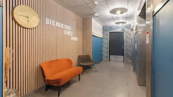 Un interior moderno con una recepción, un reloj, una pared azul y una zona de estar.