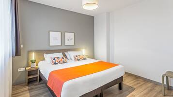 A modern hotel room with a large bed, a bedside table with a lamp, and a small plant.
