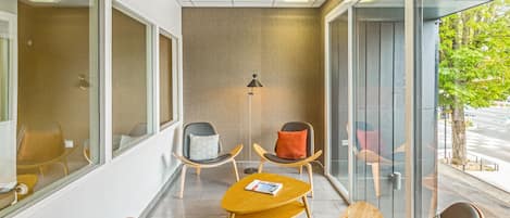 A modern waiting area with glass walls, comfortable seating, and a floor lamp.