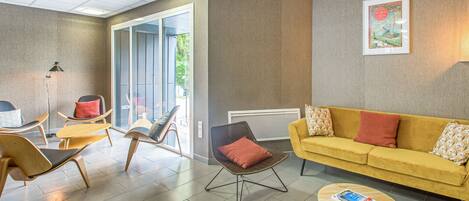A modern living room with a yellow sofa, wooden chairs, and a coffee table.