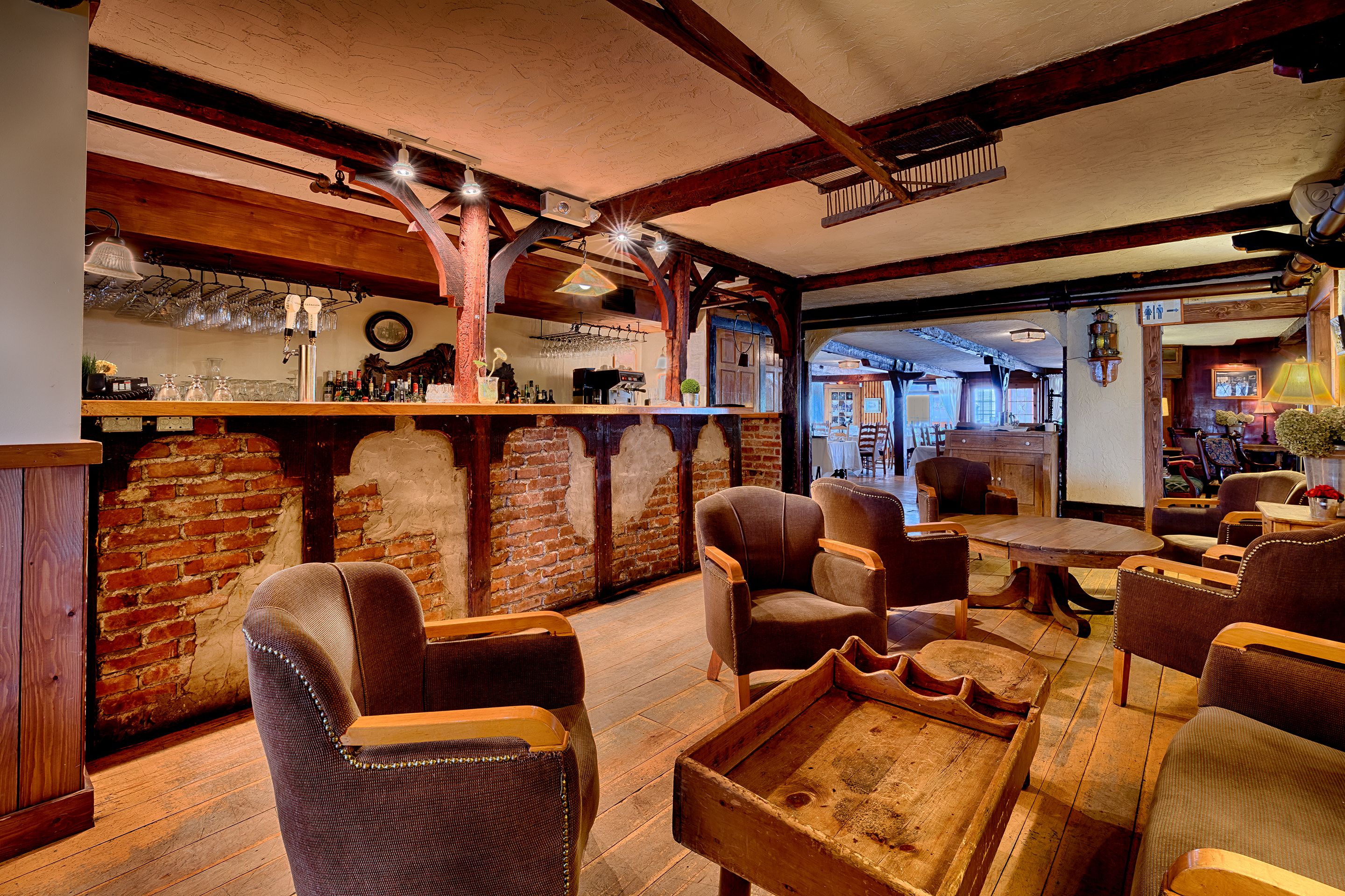 A rustic bar area with wooden furniture, brick walls, and exposed beams.