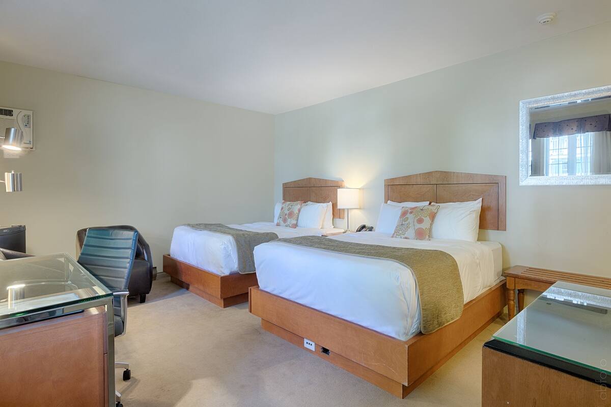 A hotel room with two beds, a desk, a chair, and a window.