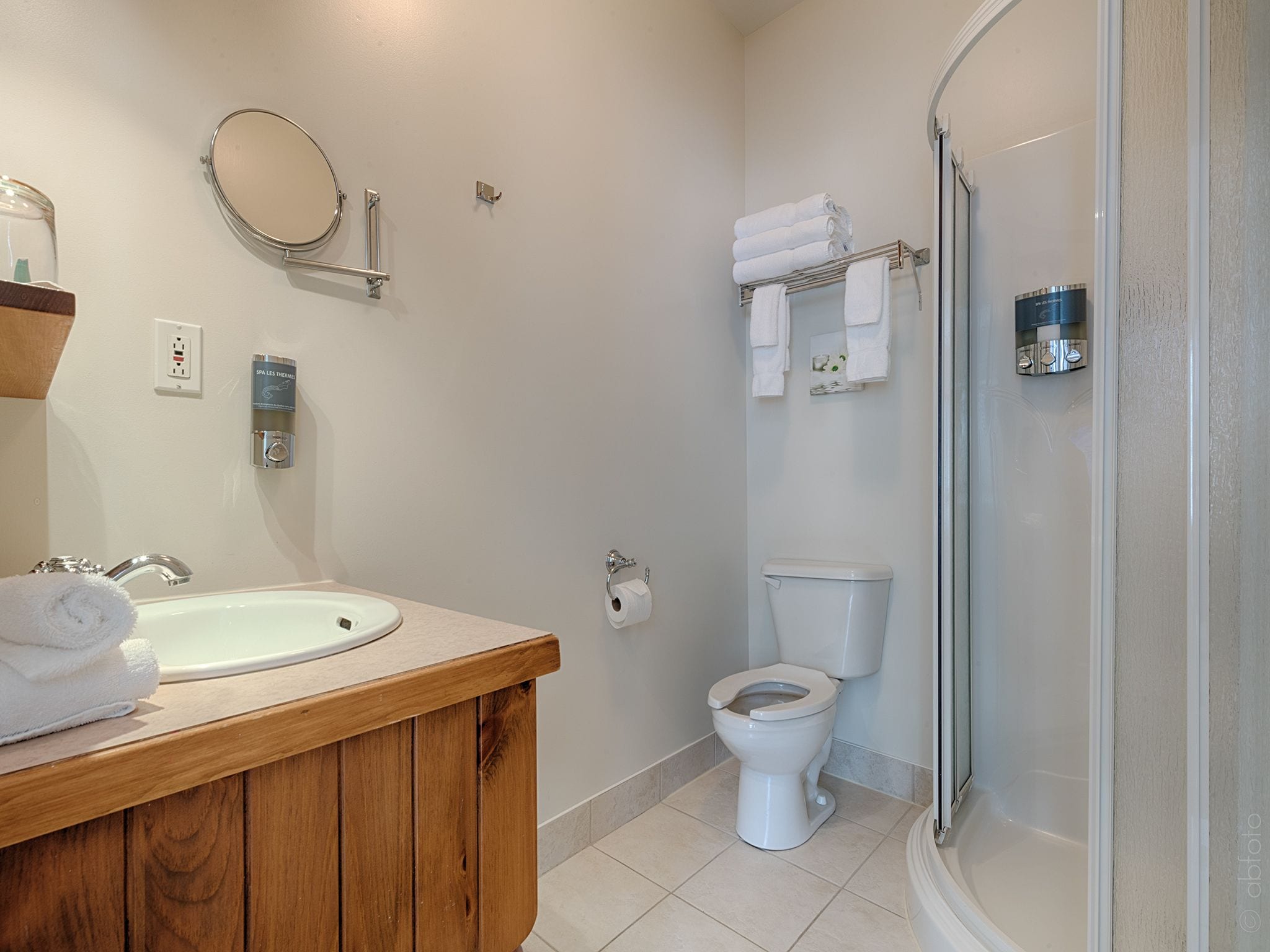 A bathroom with a wooden vanity, a round mirror, a toilet, and a shower area.