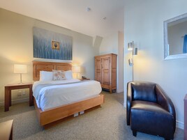 Una habitación de hotel con una cama grande, dos lámparas de noche, un armario de madera, un sillón de cuero y un cuadro en la pared.