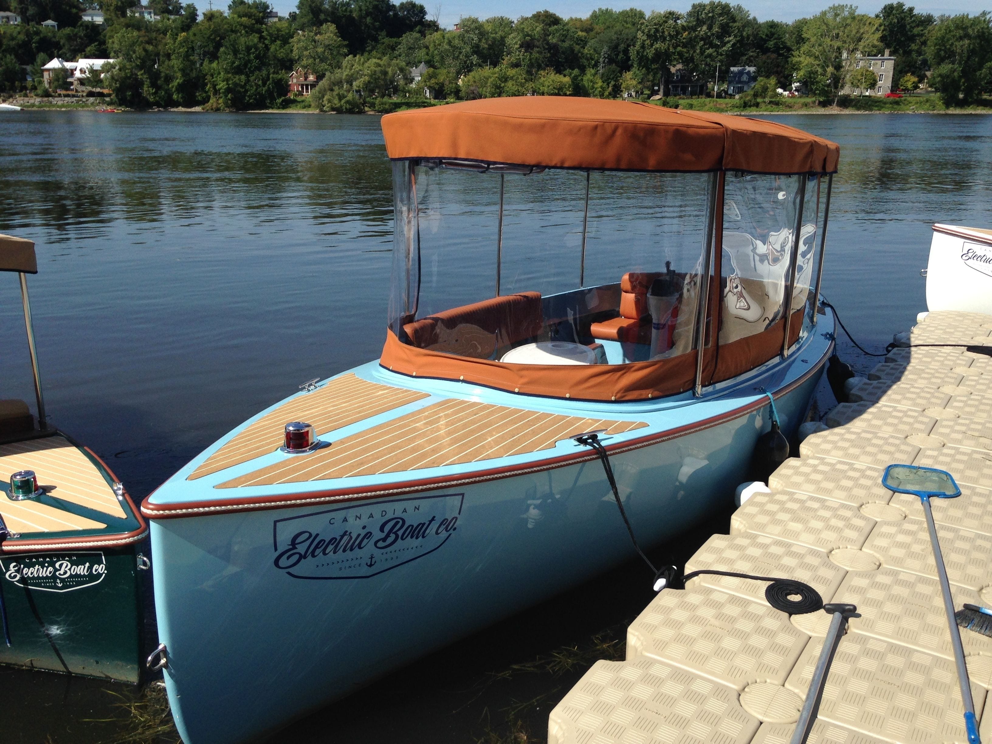 Un barco eléctrico azul con toldo marrón, amarrado a un muelle.