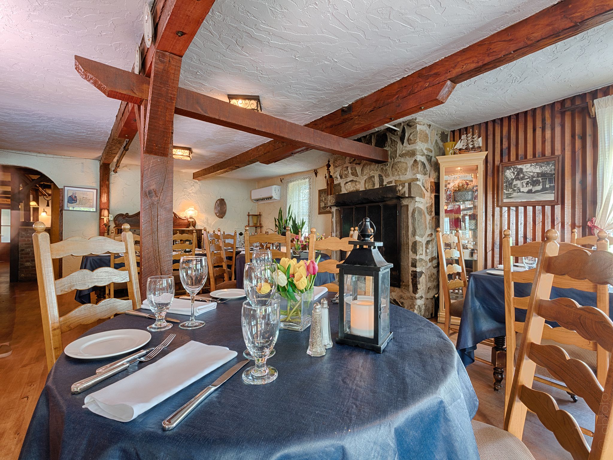 A dining area with a round table set for four, wooden chairs, and a stone fireplace in the background.
