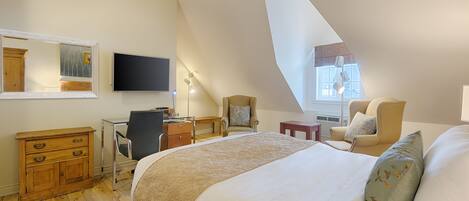 Un dormitorio con una cama grande, un escritorio, una silla, un aparador, un televisor y una ventana con luz natural.