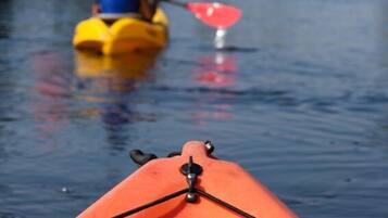 A kayak on a calm body of water with a person paddling in the background.