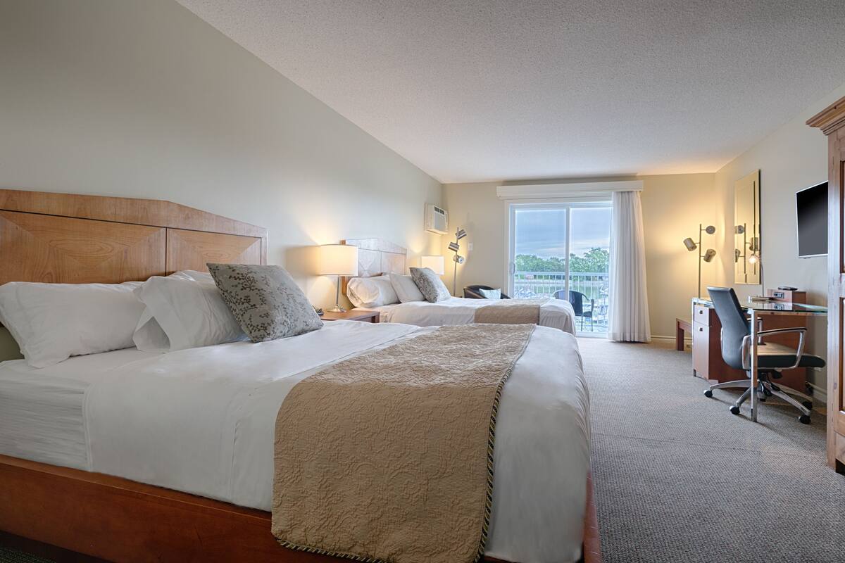 A hotel room with a large bed, a desk, and a chair. There is a window with a view of the outside.