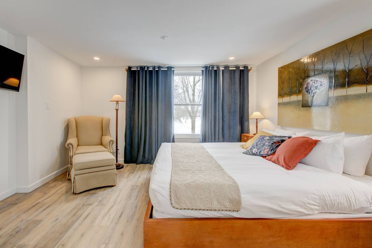 A hotel room with a bed, a chair, a painting, and a window with curtains.