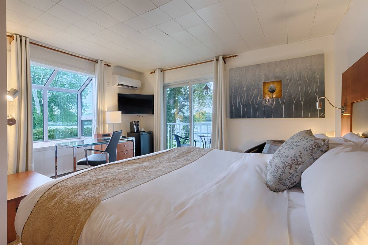 A hotel room with a large bed, a desk with a chair, a TV, and a view of trees through the window.