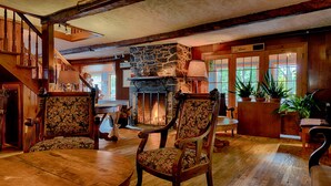 Una habitación amplia con chimenea de piedra, suelo de madera y dos sillones tapizados.