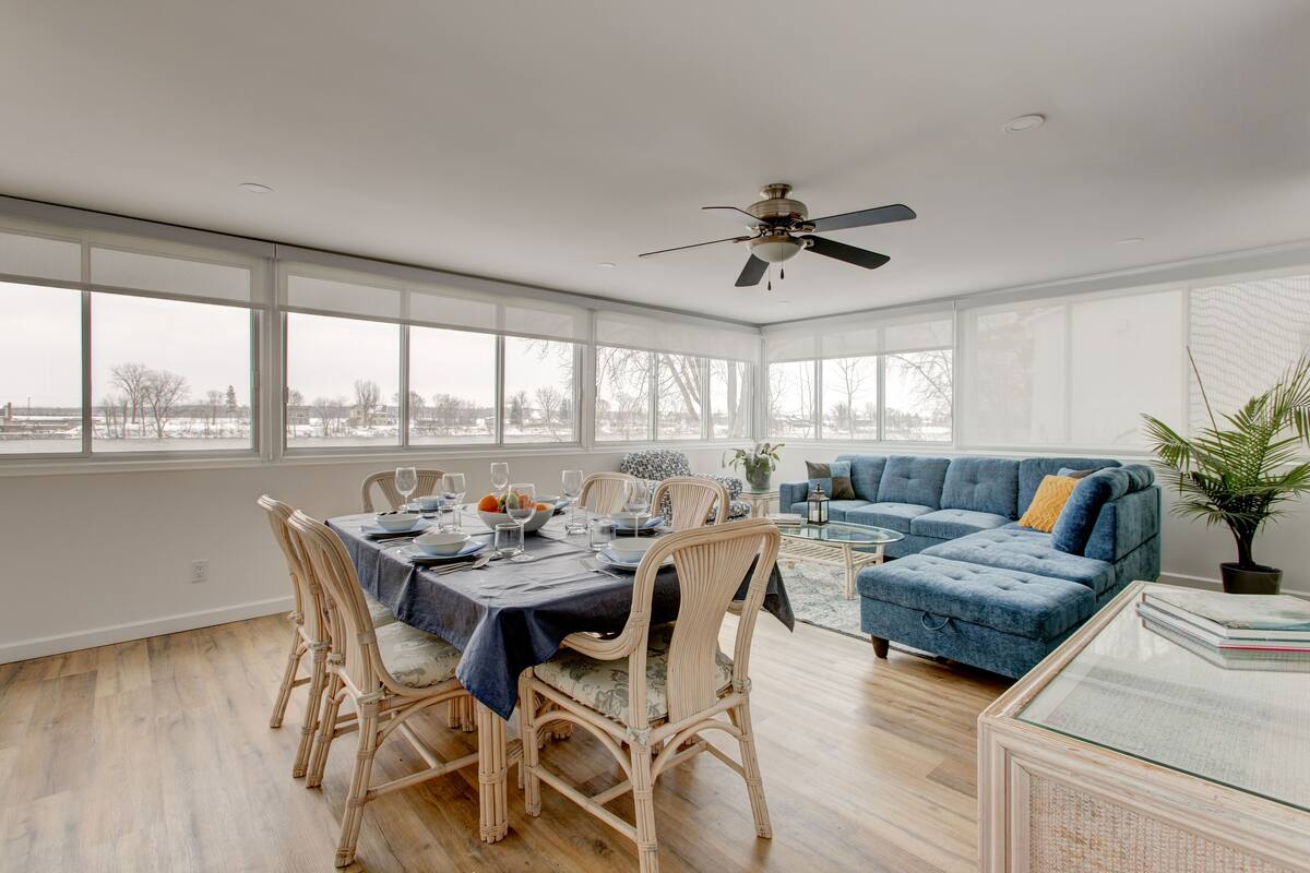 A spacious living room with a dining area, large windows, and a ceiling fan.