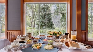 Un bufé de desayuno con diversas opciones de comida y una cafetera, frente a una ventana con vistas a árboles.
