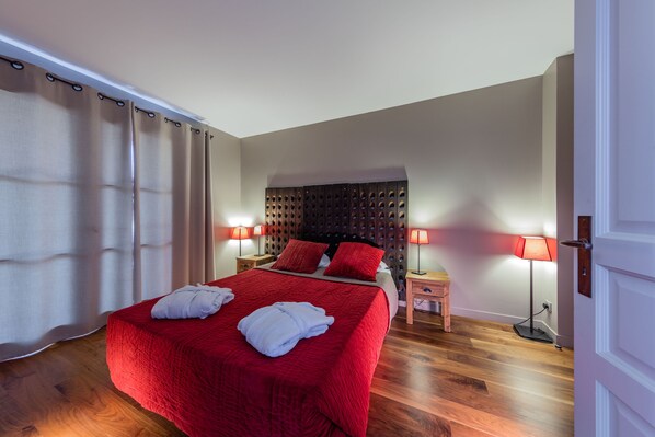 A hotel room with a large bed, two bedside tables with lamps, a wooden headboard, and a wooden floor.