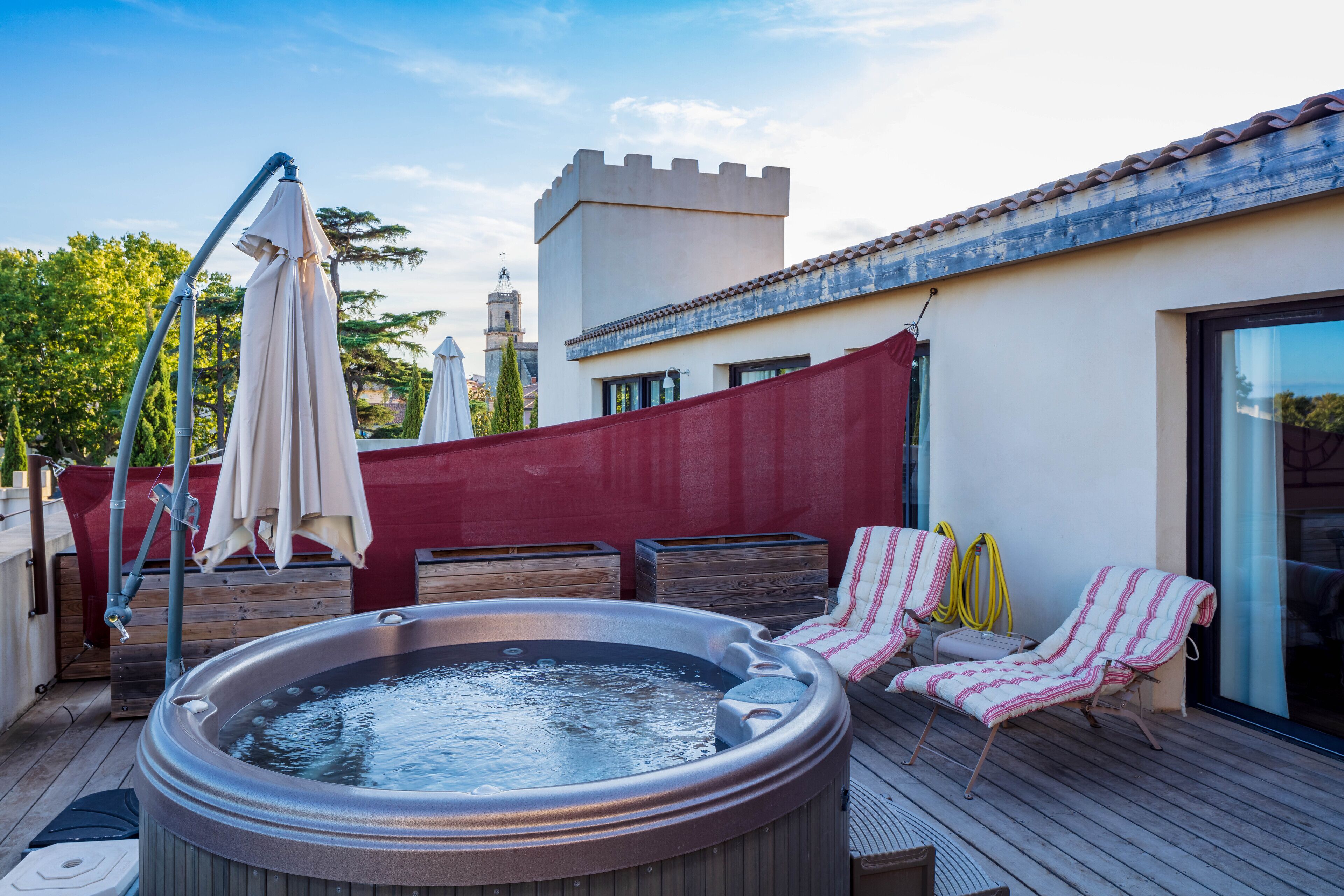 Un jacuzzi en una terraza de madera con sillones de descanso y sombrillas.