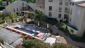 Un patio con piscina, mobiliario exterior y un edificio de piedra con varios balcones.