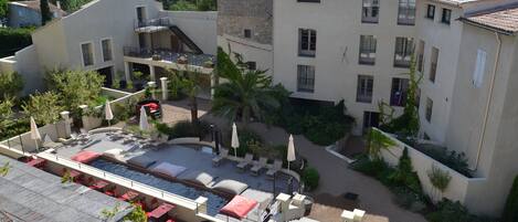 Un patio con piscina, mobiliario exterior y un edificio de piedra con varios balcones.