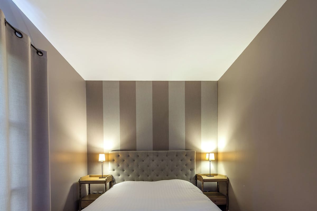 Un dormitorio con una cama grande, dos mesitas de noche con lámparas, suelo de madera y paredes a rayas.