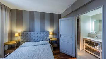 Une chambre d’hôtel comprenant un lit, des tables de chevet, une lampe, une armoire et une salle de bain avec un miroir et un lavabo.