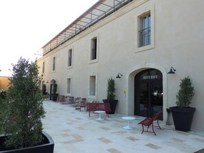 Un edificio con un letrero que dice 'BISTROT', mesas y sillas en la terraza, plantas en macetas y un patio con baldosas.
