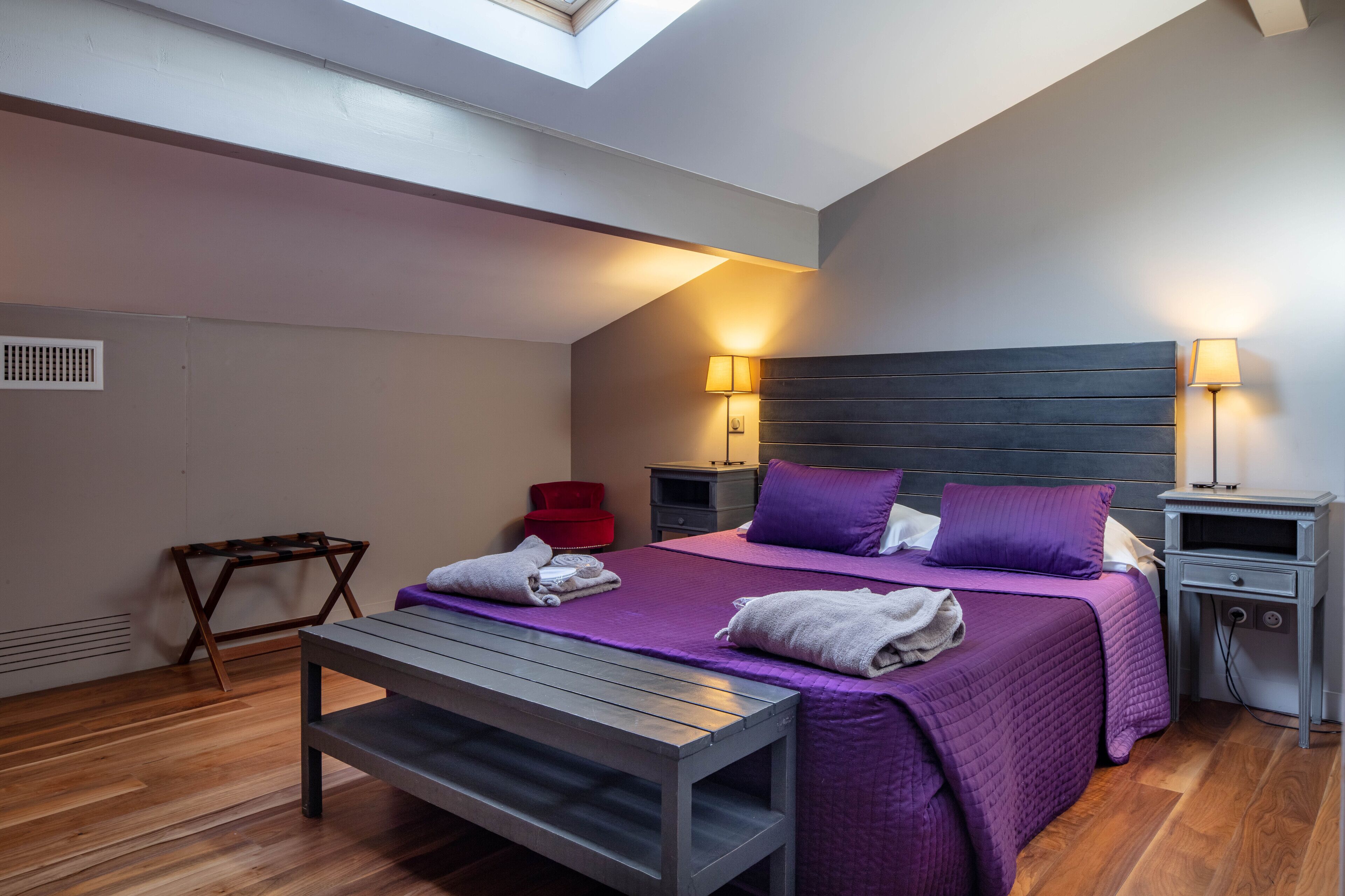 Een slaapkamer met een bed, nachtkastjes, een bankje en een dakraam.
