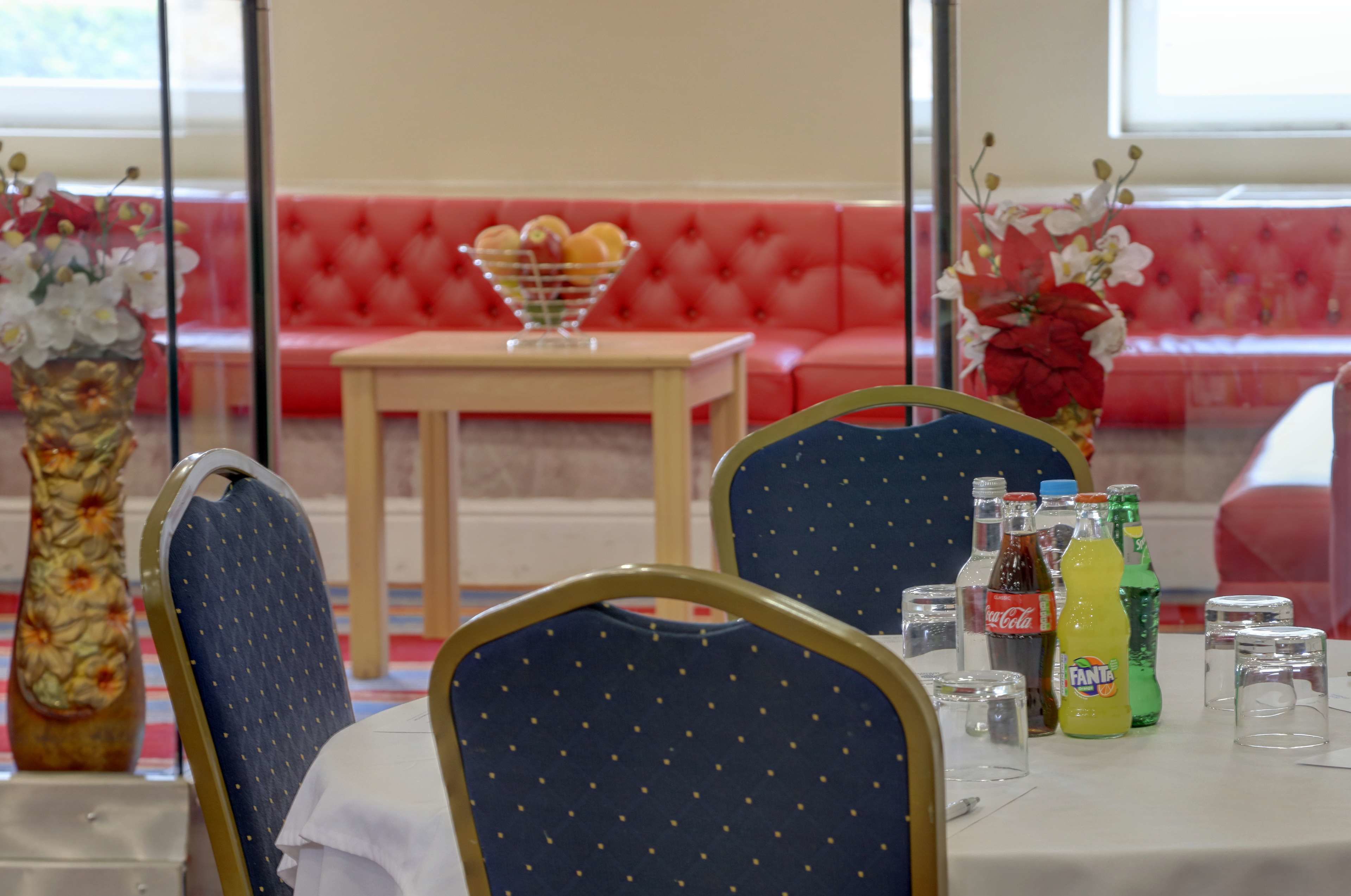 A dining area with a table set for two, featuring a vase of flowers, a bowl of fruit, and a selection of beverages.