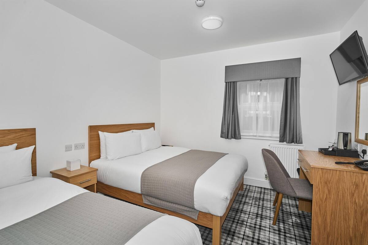 A hotel room with two beds, a desk, a chair, a television, and a window with curtains.