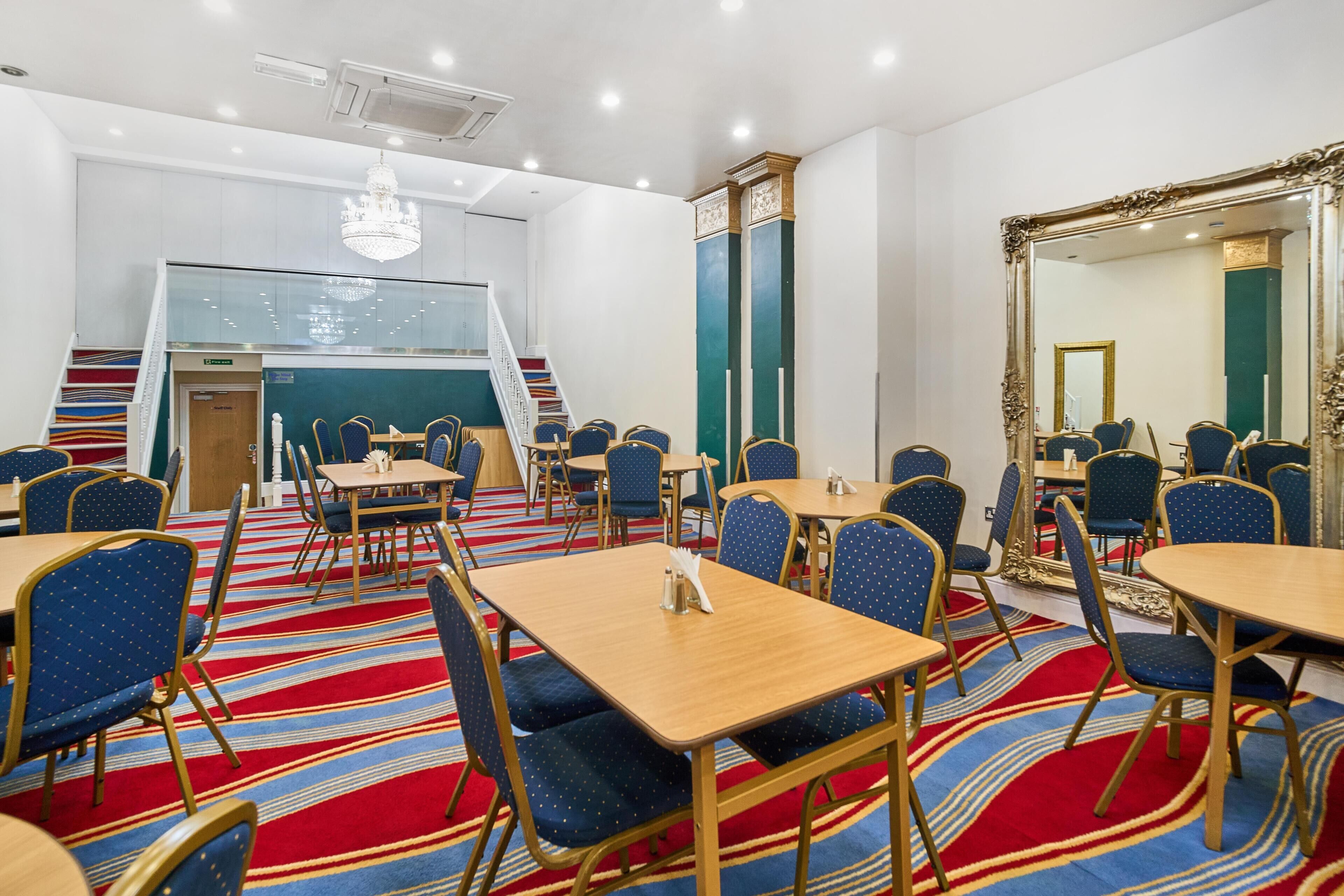 A hotel room with a staircase, multiple tables and chairs, a chandelier, and a large mirror.